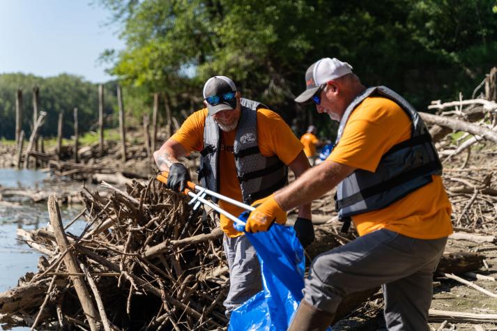 two men cleaning brush from river