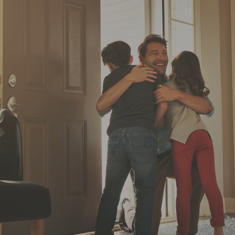 Image of father walking into the door and hugging his children